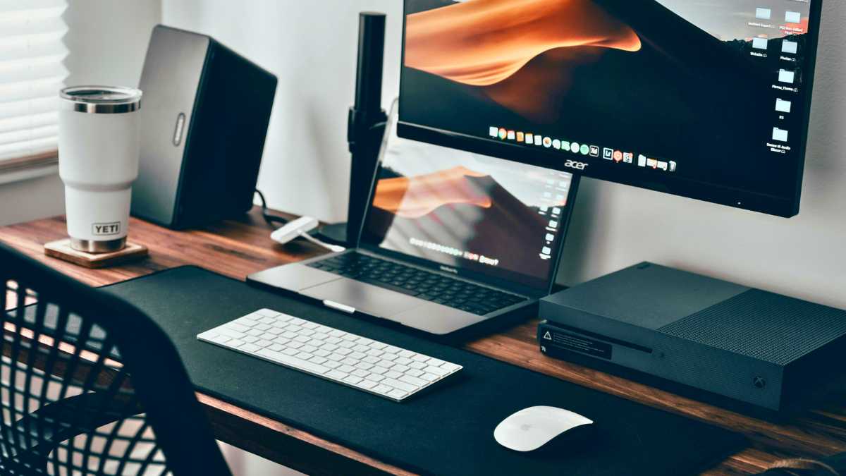 a home office desk with a macbook, a monitor, and xbox console